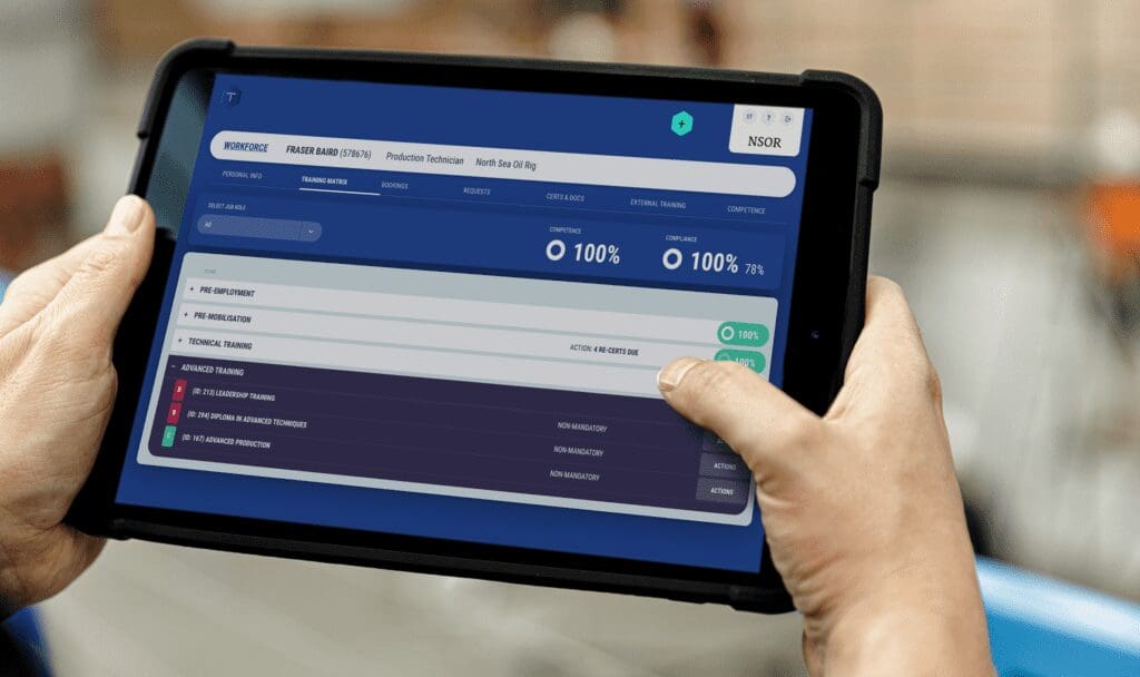 Hands holding a tablet display a digital interface showcasing training progress. The screen boasts a 100% completion rate for "Essential Training" with options for "Advanced Training" listed below—ideal for an energy investor keen on expanding expertise. The background remains elegantly blurred.