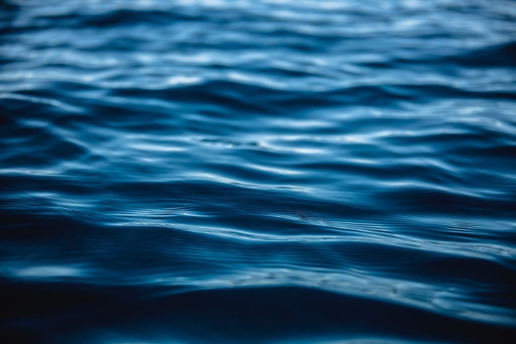 Close-up of gentle ripples on a body of water under natural light. The surface appears calm with patterns of waves reflecting shades of blue and hints of sunlight, captivating the attention much like an energy investor spotting new opportunities.